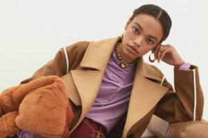 Alexis Sundman, a pretty model with a light brown complexion with her hair tied back, tilts her head and toys with an earring. She looks casual but cool in her brown wool coat and purple blouse.