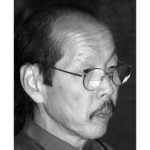 A black and white photograph of Frank Ching in profile. He has a mustache and round glasses.