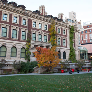 The South-Facing edifice of Carnegie Mansion, home of Cooper Hewitt. In the garden, the leaves are starting to turn orange. A few autumn leaves are on the ground.