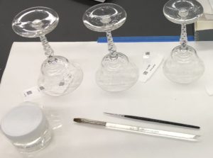 A photograph of three wine glasses on a table. They are inverted and accompanied by barcodes and paintbrushes.