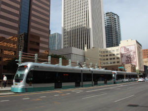 In an urban metropolis, a sleek silver and teal commuter train pulls into a station