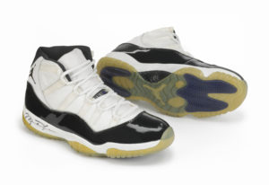 Sneakers with white uppers rimmed with black. The soles are the pale yellow of industrial plastic. The shoes have Michael Jordan's signature on the side of the heel. The silhouette of Michael Jordan soaring through the air and about to make a slam dunk are on the back of the sole
