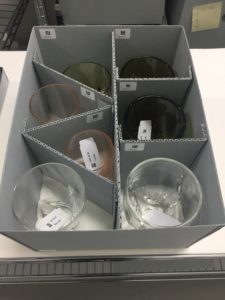 A box sits on a table. The box contains seven drinking glasses, each separate from the others by a piece of archival cardboard.