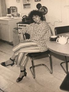 A black and white photograph of a woman seated cross-legged at a kitchen table