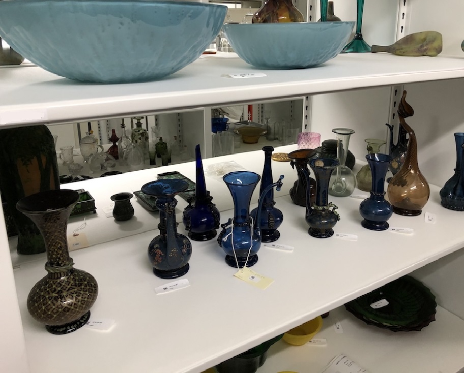 Two shelves in a storage facility contain dozens of glass vessels.