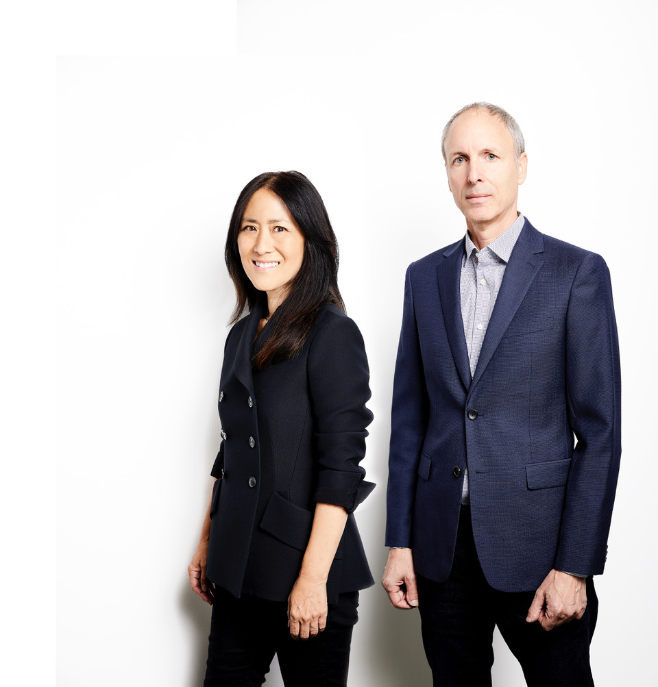 Two architects in business clothing. Lisa is a smiling Asian-American woman in her thirties. Craig is a tall white man with short white hair