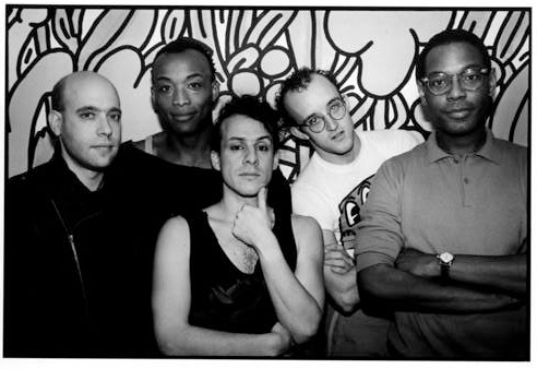 A black and white photograph of a group of people, including Keith Haring and Willi Smith, facing the camera in front a mural