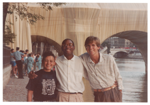 Willi Smith with two friends smiling for the camera in front a bridge wrapped in tan fabric