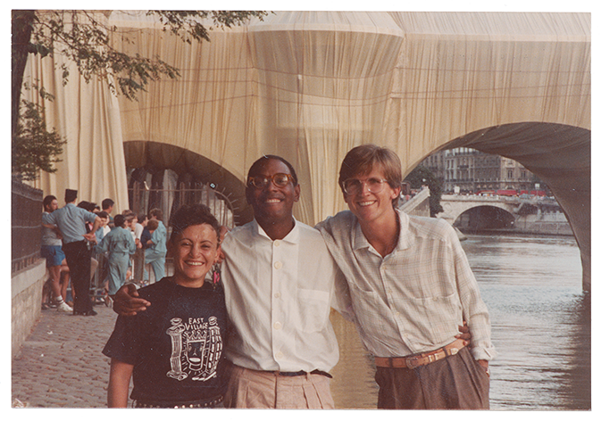 Willi Smith with two friends smiling for the camera in front a bridge wrapped in tan fabric