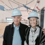 Barbara and Mort in the galleries of Cooper Hewitt smiling and wearing blue hard hats