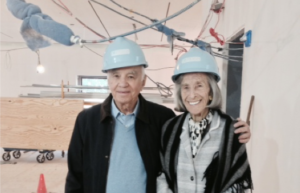 Barbara and Mort in the galleries of Cooper Hewitt smiling and wearing blue hard hats