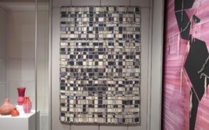 A large textile with a grid of blue, purple and white squares is shown in a gallery display.
