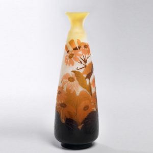 Image features a tall conical vase with a narrow neck and flaring mouth, the opaque glass body showing peach- and amber-colored flowers on a yellow to deep crimson background. Please scroll down to read the blog post about this object.