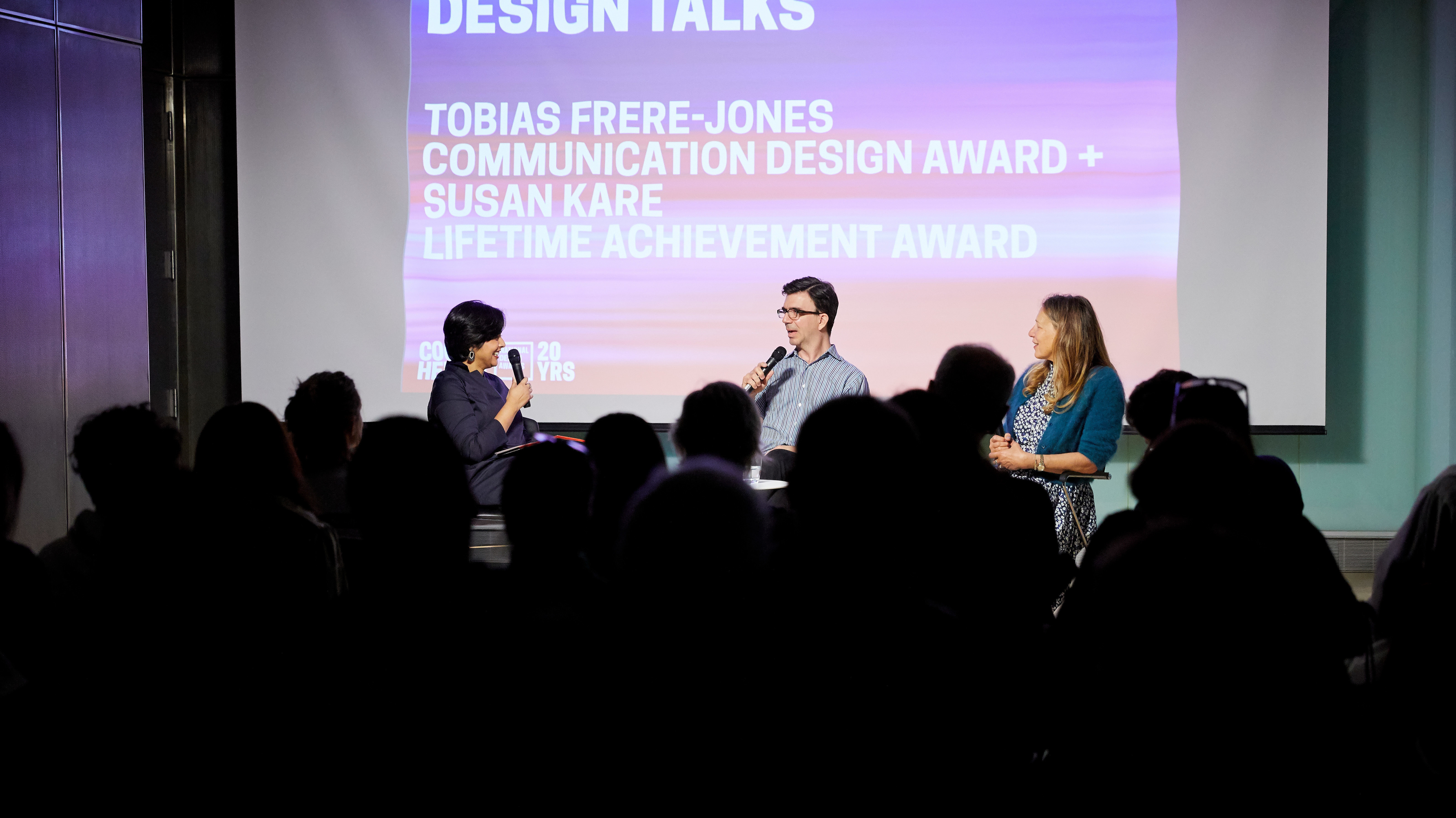 Image of three people on a stage: from the left, Ruki Neuhold Ravikumar has dark short hair and holds a microphone, in the middle Tobias Frere-Jones wears a blue shirt, dark glass, and has dark hair, on the right, Susan Kare, wearing a blue patterned dress and dark blue sweater, her hair is golden brown