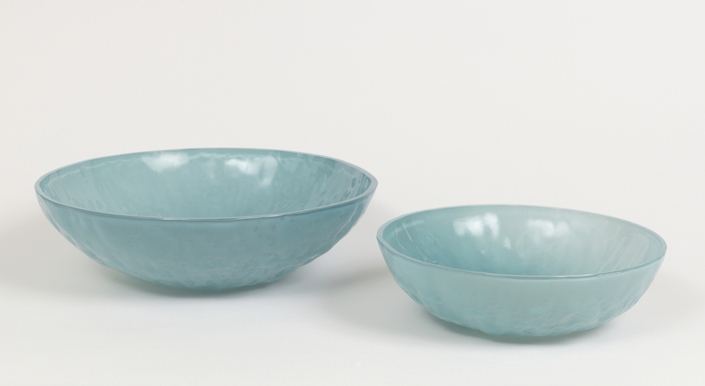 Image features two circular bowls, one smaller than the other, made of translucent aqua-toned glass, their surfaces showing the textures and irregularities of the stone molds used to shape them. Please scroll down to read the blog post about these objects.
