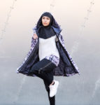 A model runs in place.She wears a black hijab, a purple slicker coat with hood, a white tunic that ends with a stripe of fabric matching the coat, baggy black pants with a sporty stripe on one side, and white running sneakers. Her face is determined and serious.