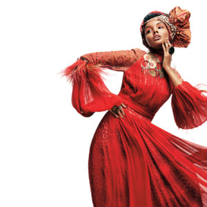 A glamorous model wearing a flowing red gown and a large hairwrap strikes a pose