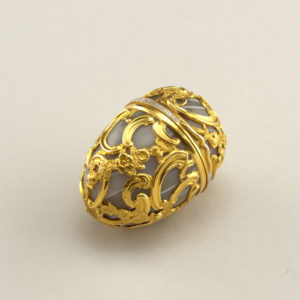 Egg-shaped form of curving rococo gold cage work over gray agate. Hinged lid with white enameled band showing the phrase, "Eloignez de vous rien n'est agreable" (Separated from you nothing is pleasant).