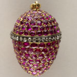 In the shape of an egg with red stones and a single dark band with clear stones in the middle with a clasp on the top.