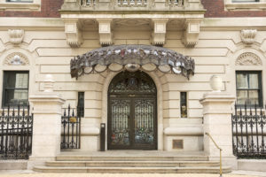 The facade of Carnegie Mansion, which features an elegant brass and glass Tiffany canopy over the front doors. This image has been digitally altered to contain 10 hidden objects that are shaped like eggs.