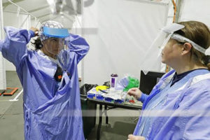 Two medical workers in scrubs try on the Design that Matters mask in a white tent.