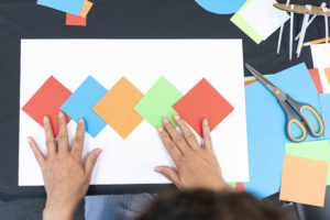 A pair of hands arrange square sheets of paper, all different colors.