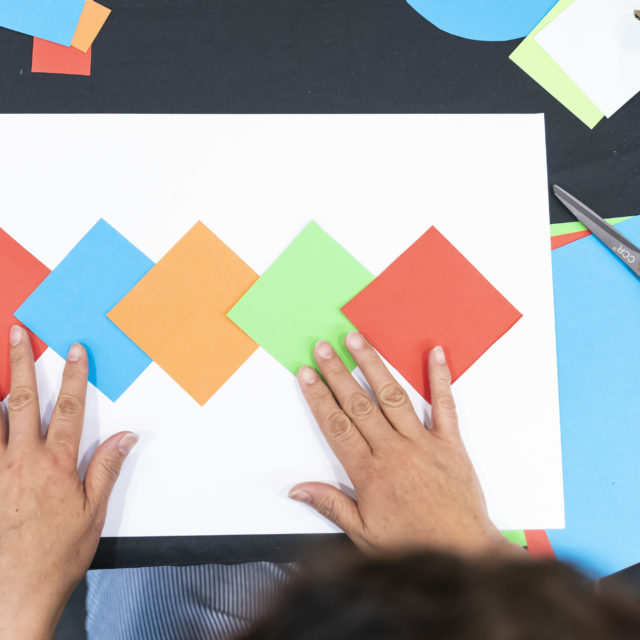A pair of hands arrange square sheets of paper, all different colors.