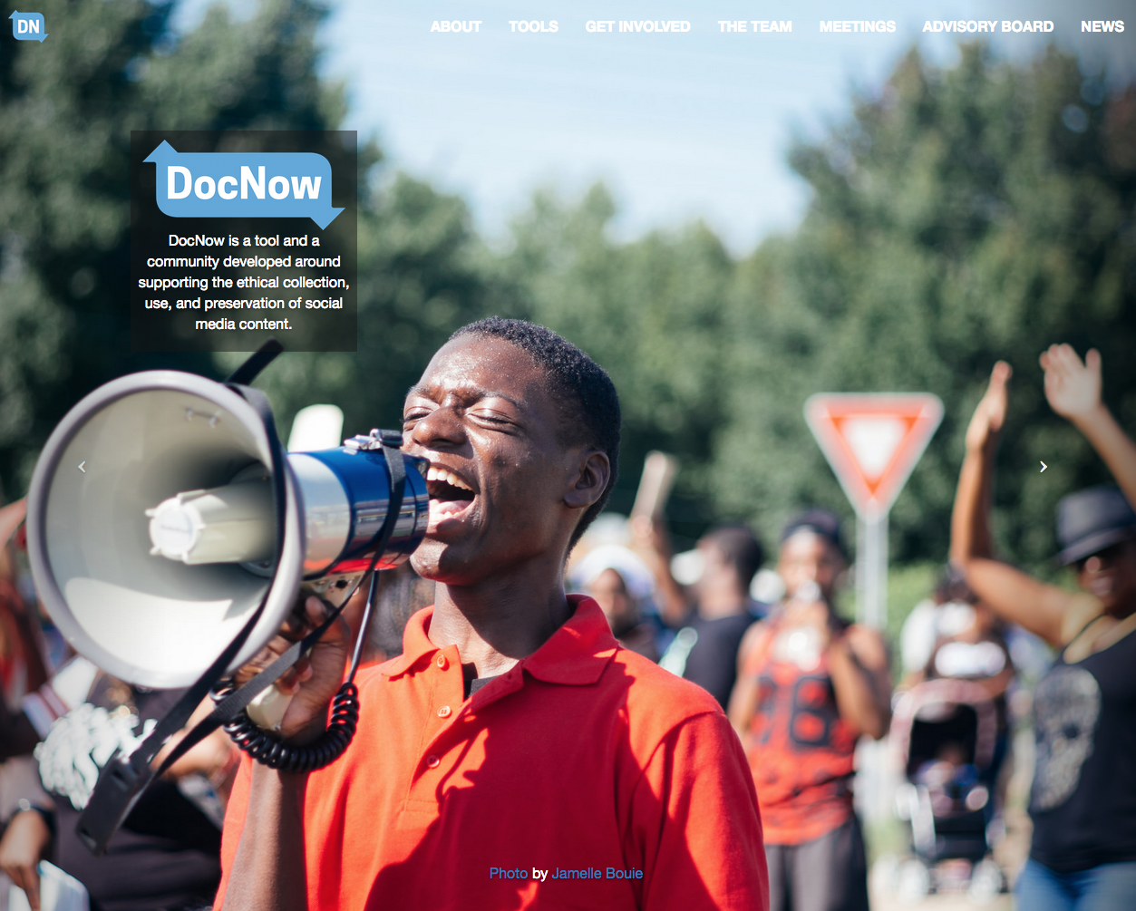 A crowd gathers behind an African American man shouting into a megaphone. Superimposed on this image is the logo for the DocNow project.