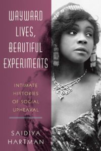 Book cover Wayward Lives, Beautiful experiments intimate histories of social upheavel by Saidiya Hartman. The book cover shows a black and white photograph of a young African American woman with flowing wavy hair wearing a beadde crown, long beaded earrings, a delicate neckalce, and a romantic ruffly gown. She looks wistfully to the right.