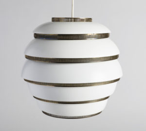 Image features a white-enameled beehive-shaped hanging lamp divided into five horizontal segments by perforated brass bands. The lamp hangs from a white cord at center top. Please scroll down to read the blog post about this object.