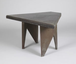 Image features a low table consisting of a triangular top on two angled, panel-form legs tapering to small feet, the entire form covered in dark brown patinated copper. Please scroll down to read the blog post about this object.