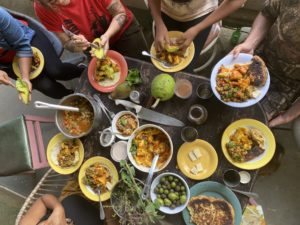 An aerial image showing people engaging with a table full of food, brightly colored bowls.