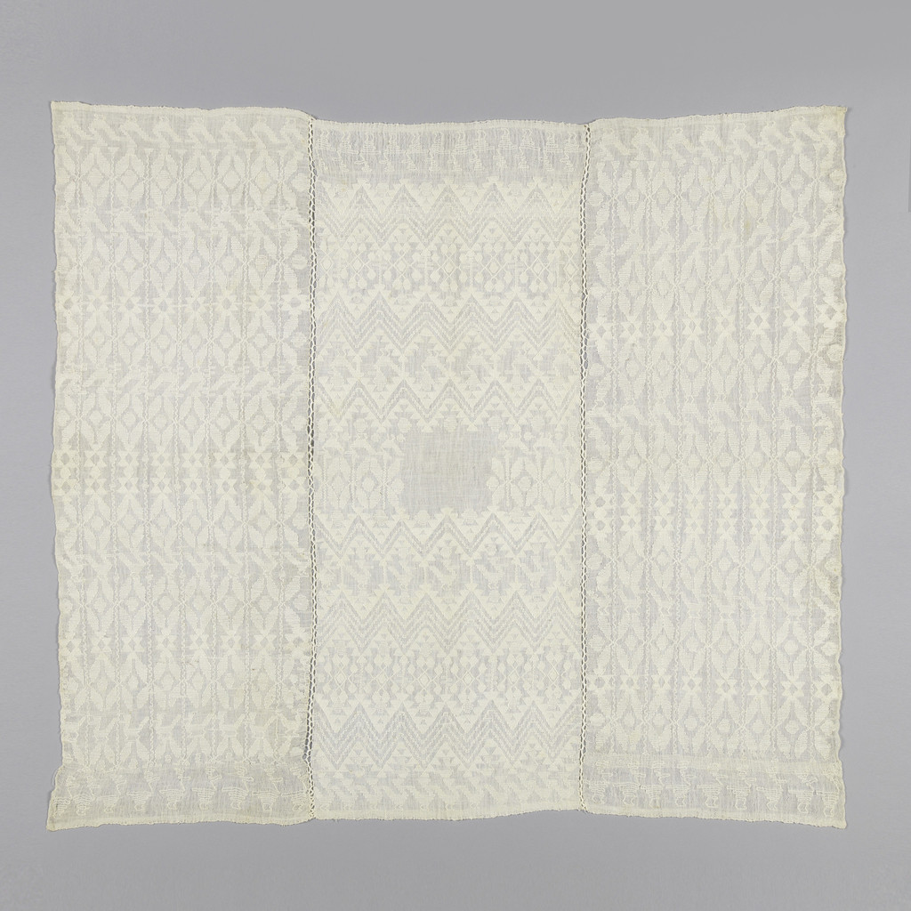 Image features: Three white-on-white patterned textiles sewn together, each having four selvages. The two outer textiles are patterned with stripes of geometric shapes including a bird. The center is patterned with zigzag bands, one above the other, to form an elongated diamond shape. Head opening is uncut. Please scroll down to read the blog post about this image.