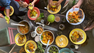 An aerial image showing people engaging with a table full of food, brightly colored bowls.