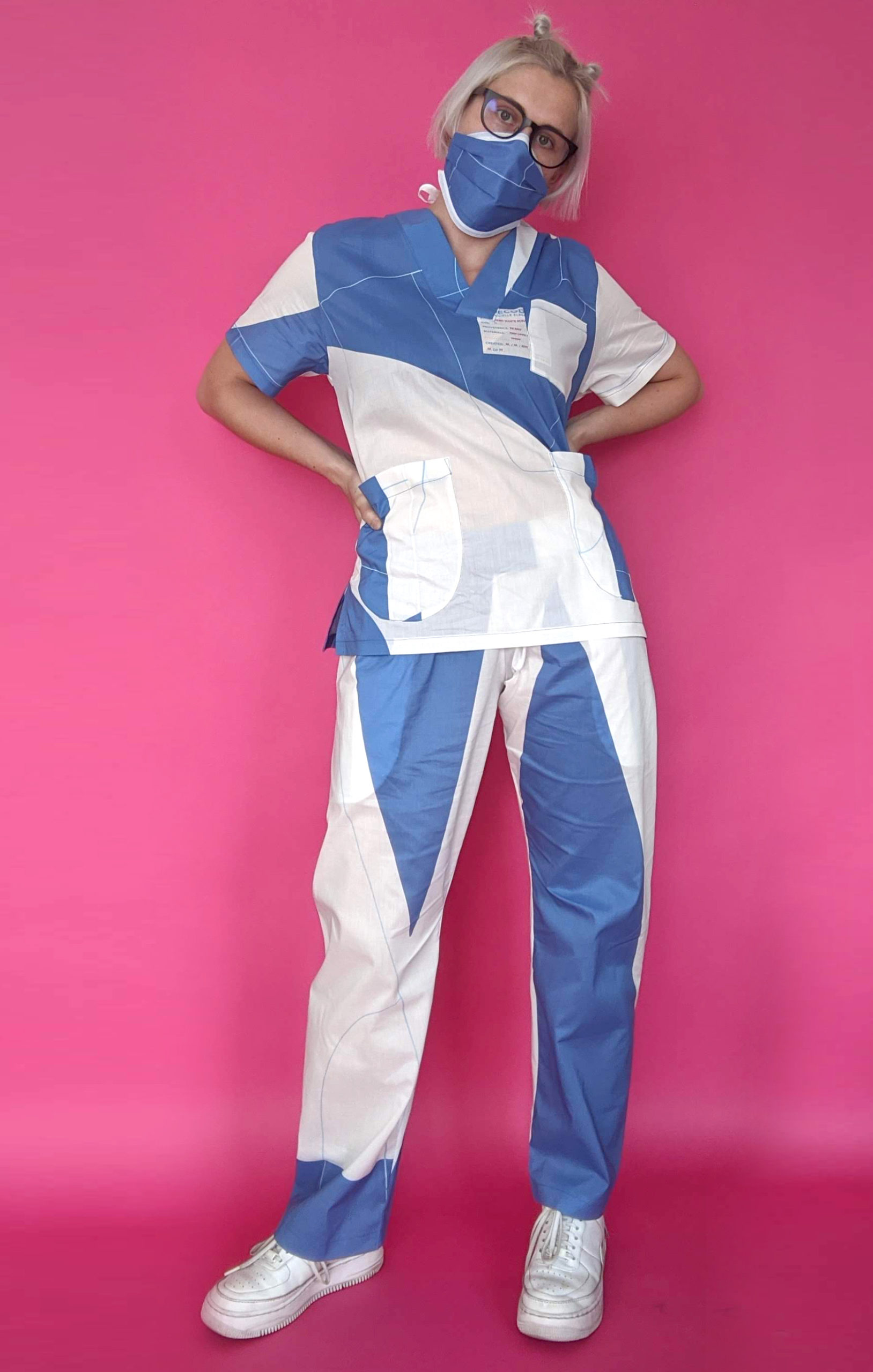 Woman in blue and white striped scrubs standing in front of a solid pink background