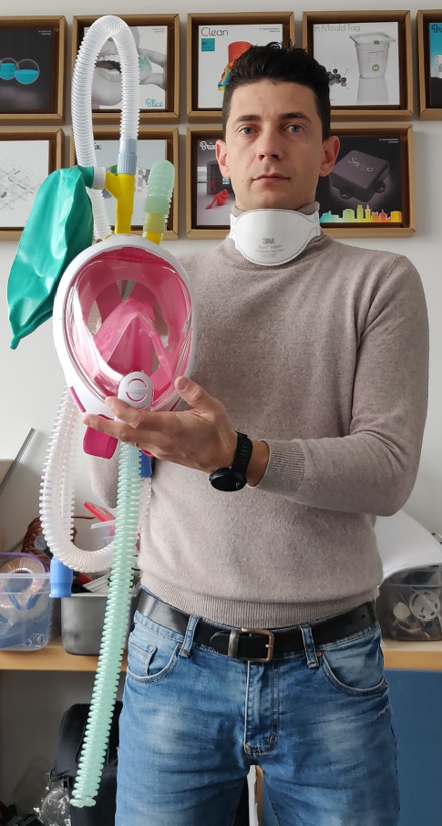 Man stands in a workshop facing the camera holding a ventilator