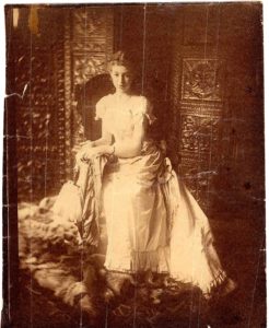 Full-body portrait of Eleanor Hewitt, seated wearing a bright, floor length dress.