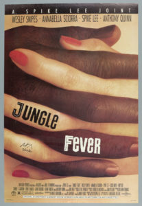 Poster for the Spike Lee film, ‘Jungle Fever.’ Features a close-up view of a dark skinned male hand entwined with a light-skinned female hand with polished red nails. A black row with white text at the top reads ‘A SPIKE LEE JOINT,’ with the primary cast members listed directly below in black: ‘WESLEY SNIPES, ANNABELLA SCIORRA, SPIKE LEE, ANTHONY QUINN.’ Film credits listed in black at the bottom of the poster. The logo for Forty Acres and a Mule Filmworks, rating information (R), and the Spectral Recording/Dolby Studio logo appear on the bottom left. The Universal logo is seen on the bottom right.