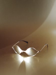 A pair of sunglasses photographed on a brown background. Light reflects off the sunglasses onto the surface giving the appearance that the sunglasses are glowing.