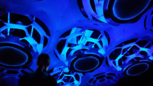 A photograph taken at an angle towards a dark blue ceiling, which features an interactive installation by Behnaz Farahi.