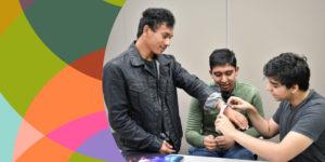 On the left side of the image is a graphic of colorful circles overlaid. On the right side, a young Project Invent student tries a prototype on a user's wrist while another student smiles and gets ready to help.