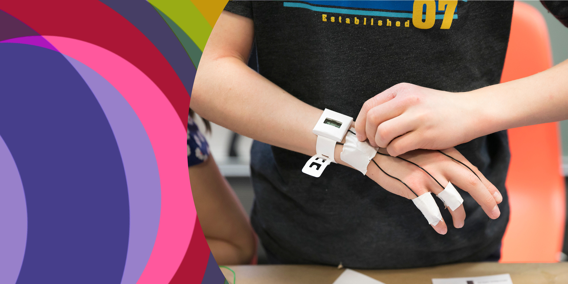 This image shows colorful, circular design elements on the left-hand border. In the center and left-hand side, the image shows a child's hands as they construct a watch on their right wrist.