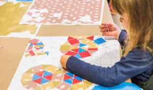 A child is creating a 2-dimensional pattern design using a range of shapes and colors.