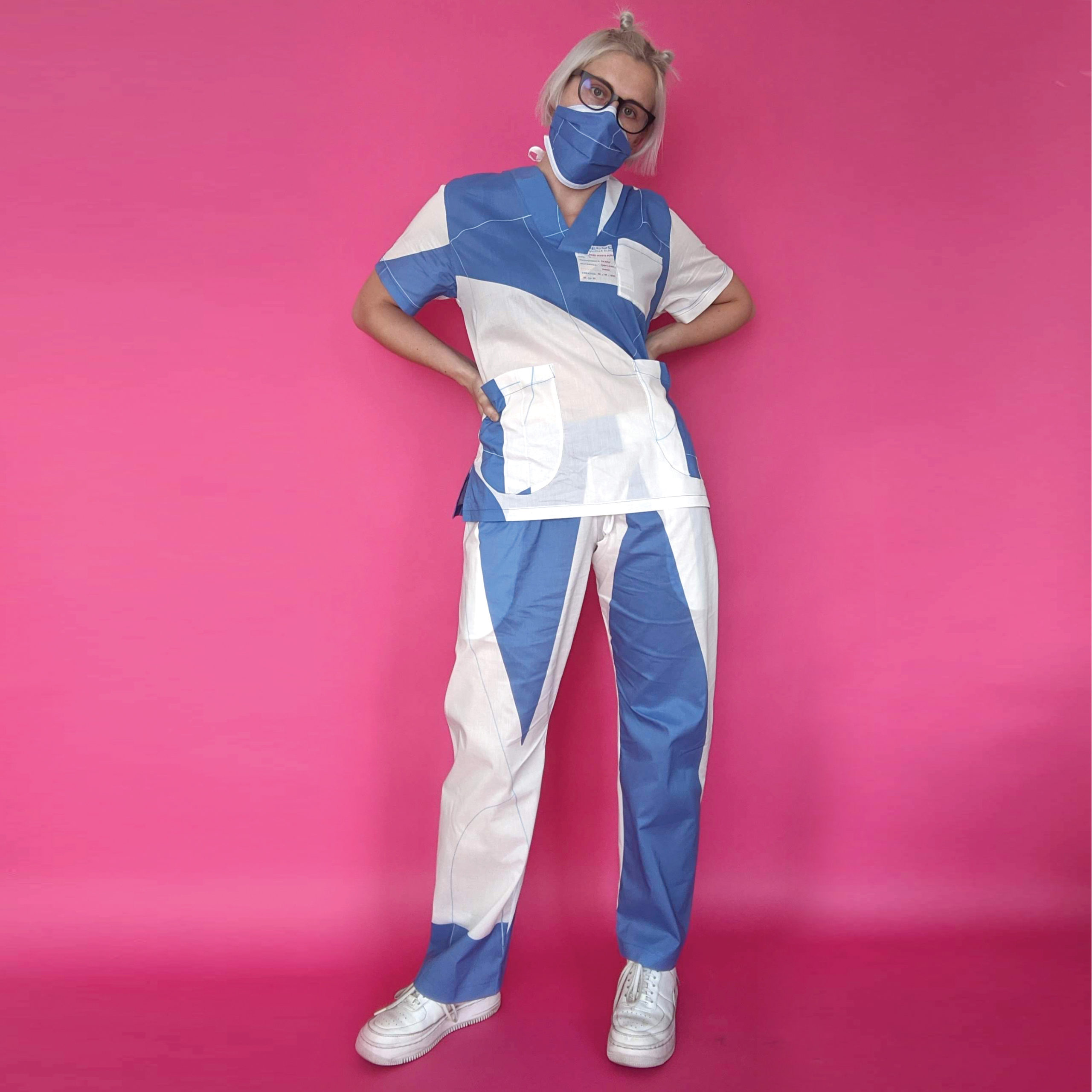 Photo of a light-skinned woman wearing a blue and white scrub set and white sneakers.