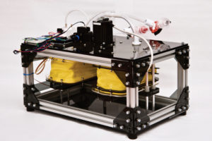 Boxy ventilator prototype with exposed electronics, wires, and circuitry; inside the open frame are four bright yellow bee bellows with metal fastenings connecting them to the rest of the apparatus