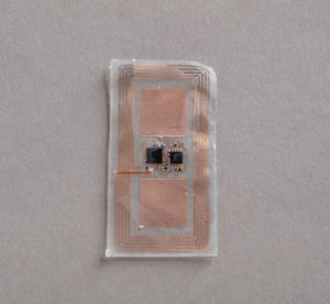 A clear rectangular rubbery sensor with bronze-colored circuitry in squiggly lines and squares