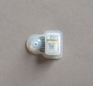 Clear rubbery sensor with a circular component at left and a rectangular one at right printed with a yellow band a sequence of numbers