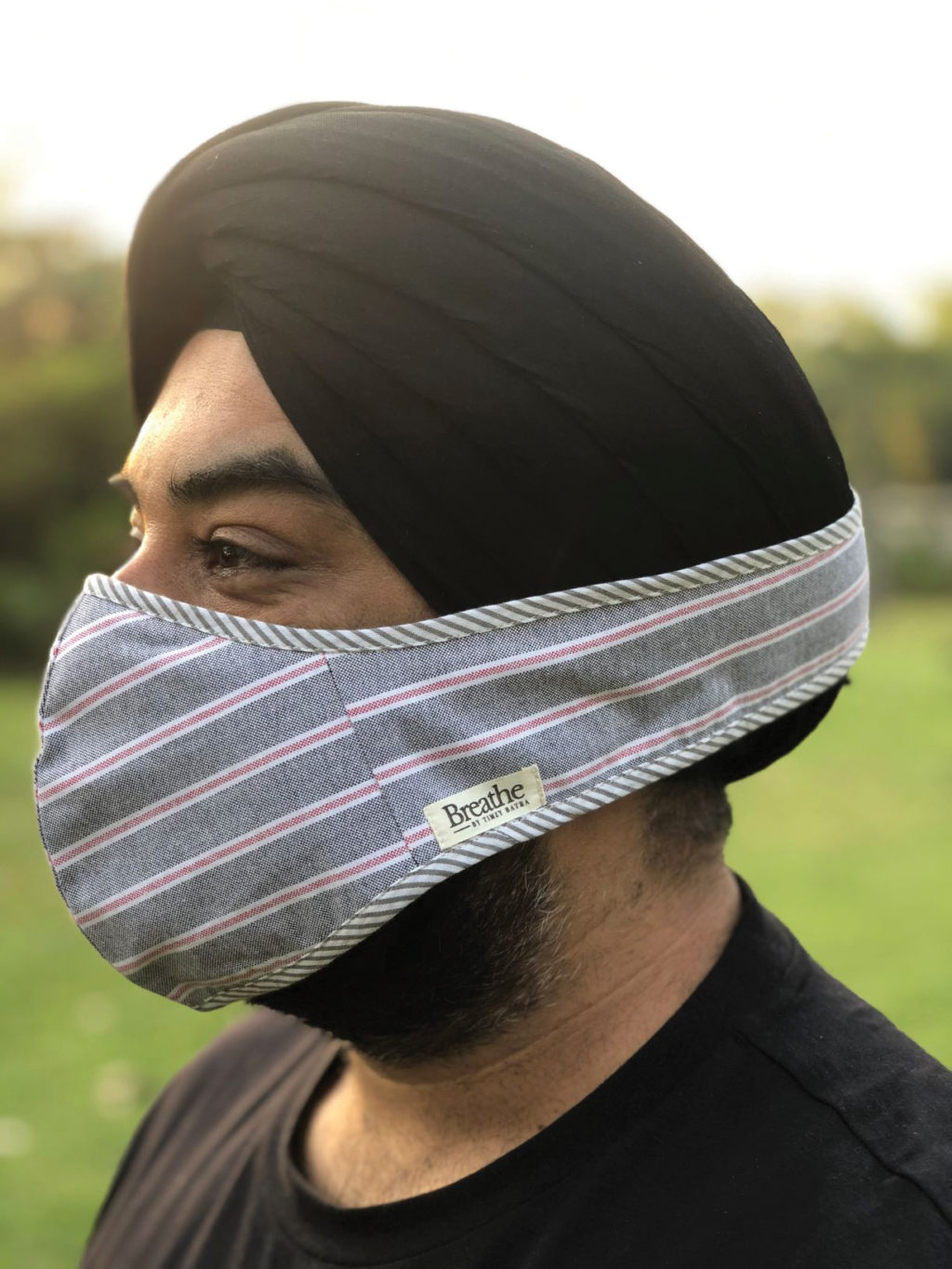 Man in profile with a gray and pink striped mask secured over lower face and a black turban