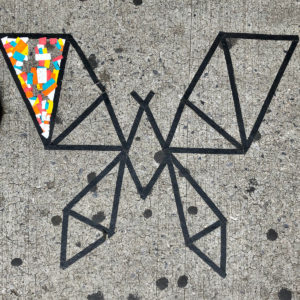 Black tape on a sidewalk forming a shape of a butterfly with a part of the left wing in color.