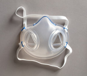Clear rubber facial respirator with two disc-shaped openings for filters and a blue metal nose bridge and elastic bands